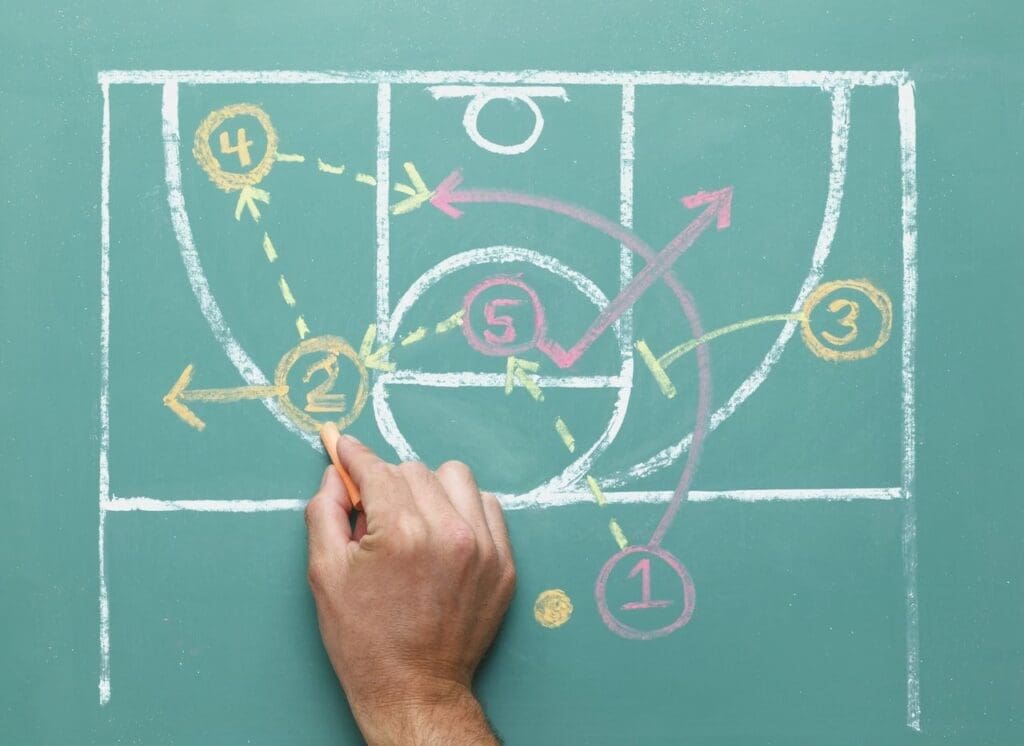 A hand is drawing a basketball play on the wall.